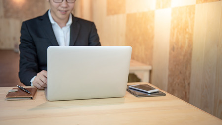 Asian businessman wearing black suit working with modern laptop computer on wooden table in the cafe. Work smart in digital age. Internet of things (IOT) conceptの写真素材