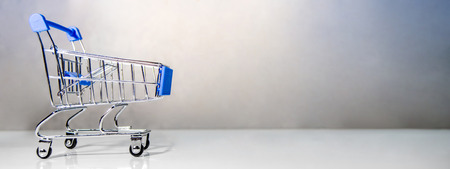 Miniature blue shopping cart or shopping trolley on the table. Supermarket grocery push cart. Banner for buying concept.の写真素材
