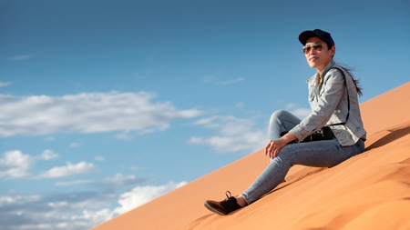 Young Asian woman traveler and photographer sitting on sand dune enjoy looking at the scenery in Namib desert of Namibia, Africa. Travel photography conceptの写真素材