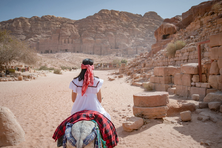 Asian woman tourist in white dress riding donkey in Petra ancient city of Jordan.の写真素材