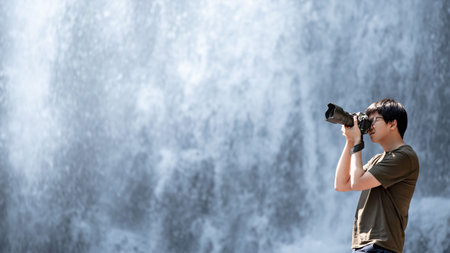 Asian man traveler and photographer using digital camera taking photo at waterfall. Travel lifestyle...