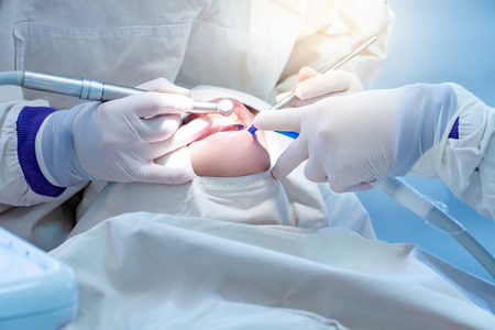 Female dentist using instrument for curing and drilling patient teeth in dental clinic. Dental procedure and medical treatment.の写真素材