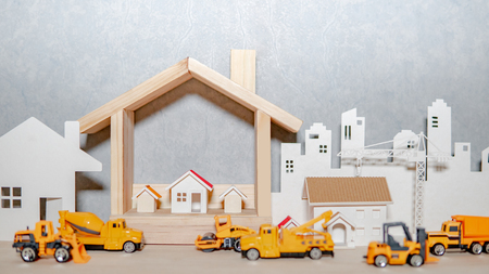 House models, paper crane and city background with miniature yellow trucks on wooden table. Architecture and construction industry for housing development business. Property or real estate conceptの写真素材