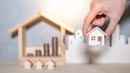 Real estate or property investment growing business. Home mortgage loan rate. Saving money for retirement concept. Male hand holding house model with blurred coin stack in house frame on the table.の写真素材