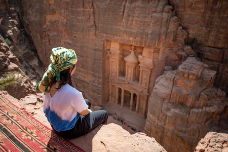 Asian woman traveler sitting on carpet viewpoint in Petra ancient city looking at the Treasury or Al-khazneh, famous travel destination of Jordan and one of seven wonders.の写真素材