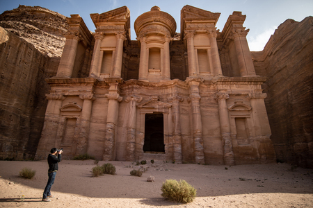 Young Asian man traveler and photographer taking photo at Ad Deir or El Deir, the monument carved out of rock in the ancient city of Petra, Jordan. Travel Middle East conceptの写真素材