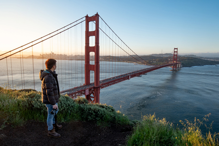 Asian man photographer and tourist enjoy looking at Golden Gate Bridge during sunrise, Iconic bridge and famous landmark of San Francisco, California, USA. Travel photography conceptの写真素材