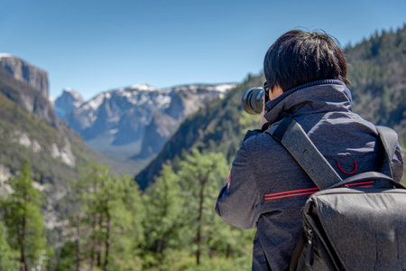 Asian man photographer and tourist with backpack holding DSLR camera taking photo of Half Dome...