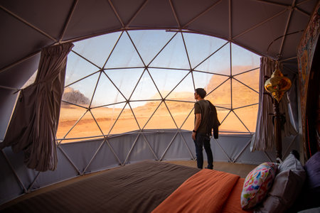 WADI RUM, JORDAN - OCTOBER 26, 2018 : Asian tourist man in dome tent looking outside at Wadi Rum desert, famous natural attraction in Jordan. Travel Middle east conceptのeditorial素材