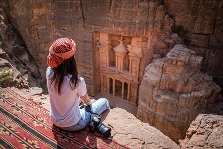 Asian woman traveler sitting on carpet viewpoint in Petra ancient city looking at the Treasury or Al-khazneh, famous travel destination of Jordan and one of seven wonders.の写真素材