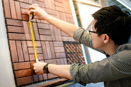 Young Asian man worker using tape measure for measuring dimension of wooden floor pavement block...