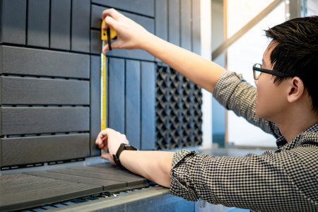 Young Asian man worker using tape measure for measuring dimension of wooden floor pavement block pattern mockup. Shopping lifestyle in warehouse conceptの写真素材