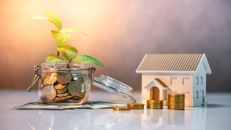 Real estate investment or property ladder. Home mortgage loan rate. Saving money for future concept. Plant growing out of coins in glass jar with dollar banknotes and house model on the tableの写真素材
