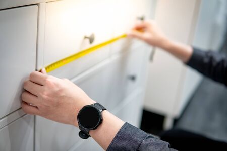 Male hand interior designer using tape measure on modern white cabinet drawer in furniture store. Home improvement conceptの写真素材