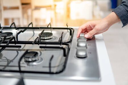 Male hand turning switch knob on modern gas stove in kitchen showroom. Cooking appliance in domestic kitchen. Home improvement and House interior design conceptsの写真素材