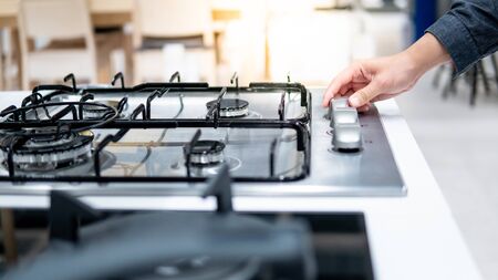 Male hand turning switch knob on modern gas stove in kitchen showroom. Cooking appliance in domestic kitchen. Home improvement and House interior design conceptsの写真素材