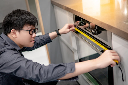 Asian man interior designer using tape measure on oven in the kitchen showroom in furniture store....