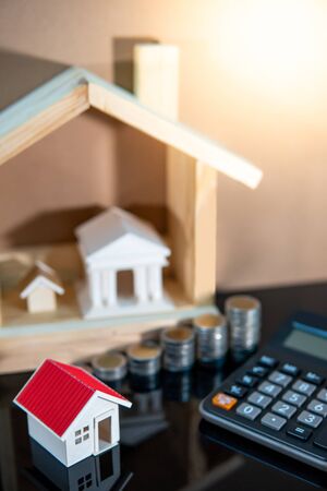 Banking concept. Loan interest rate calculation. Saving money for property investment or real estate development. Home mortgage and lease. Coin stacked, house and bank models with calculator on table.の写真素材
