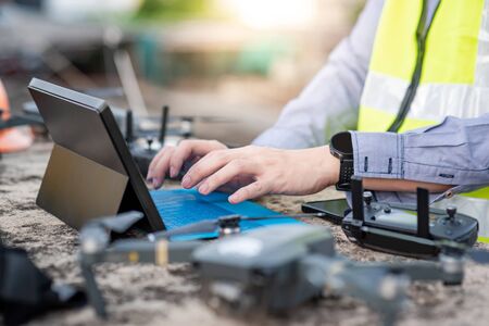 Male worker using drone, remote control and laptop computer at construction site. Unmanned aerial vehicle (UAV) for land and building site survey in civil engineering project.の写真素材