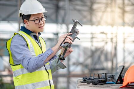 Asian engineer man working with drone, laptop and working tools at construction site. Male worker using unmanned aerial vehicle (UAV) for land and building site survey in civil engineering project.の写真素材