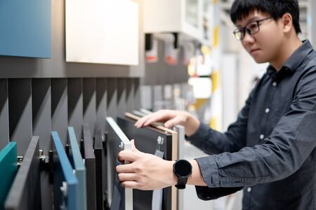 Asian man choosing cabinet panel materials or countertops for built-in furniture design. Shopping furniture and decoration. Home improvement conceptの写真素材
