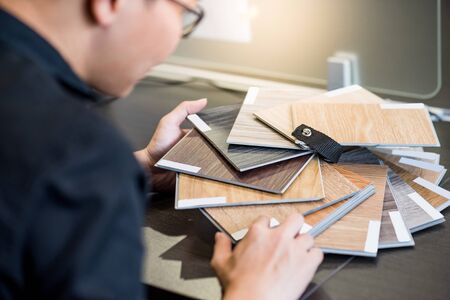Male architect or interior designer holding wooden color swatch choosing wood material for housing project. Sample of wood laminated chipboard for furniture design. Architecture and construction.の写真素材