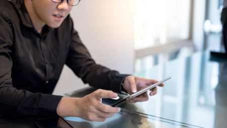 Young Asian businessman using digital tablet in office meeting room. Male entrepreneur reading news...