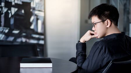 Asian businessman looking at black book on the table in public library. Education research and self improvement with printed media. World Book Day conceptの写真素材