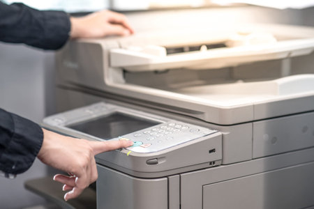 Male hand pushing button on photocopier copying and printing report paperwork in office. Electronic...