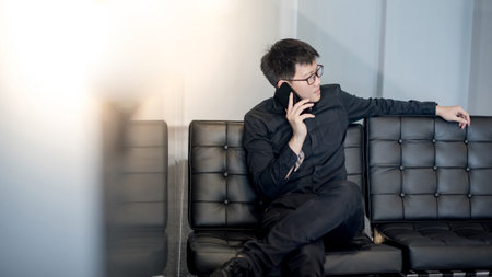 Young Asian businessman using smartphone on leather sofa in office. Male entrepreneur talking...