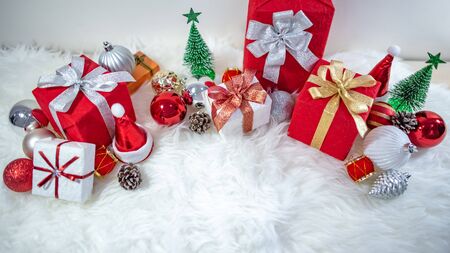 Christmas decoration on white hairy carpet. Gift box with ribbon, glossy ball, pine cone, Christmas tree and mini santa hat on fluffy rug. Present and decorative objects for New Year holidayの写真素材