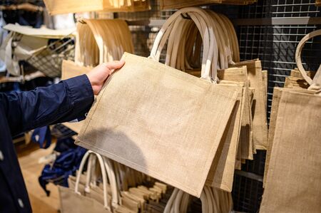 Male hand customer choosing brown jute handbag in craft shop. Reusable and Eco-friendly material bag for shopping. Buying conceptの写真素材