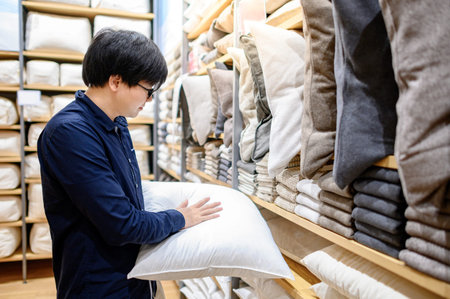 Young Asian man customer choosing throw pillow or sofa (couch) pillow in furniture store. Shopping...