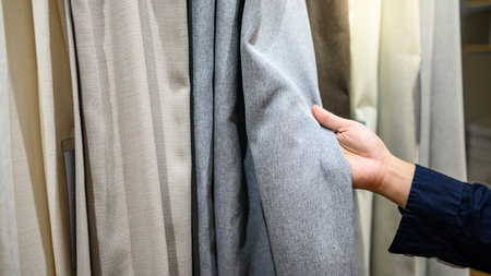 Male hand choosing color and texture of curtain samples in furniture store showroom. Interior design...
