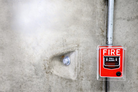Red fire alarm switch on concrete wall in office building. Industrial fire warning system equipment...