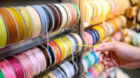 Male hand choosing Yellow Ric Rac ribbon from colorful ribbon rack in craft shop. Artisan and Handcraft conceptの写真素材