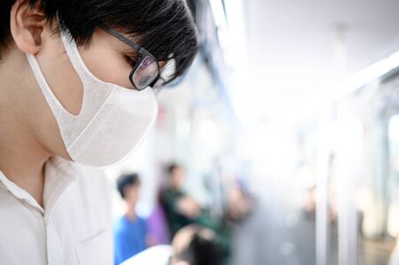 Asian man wearing surgical face mask on skytrain or urban train. coronavirus (COVID-19) outbreak prevention in public transportation. Health awareness for pandemic protectionの写真素材
