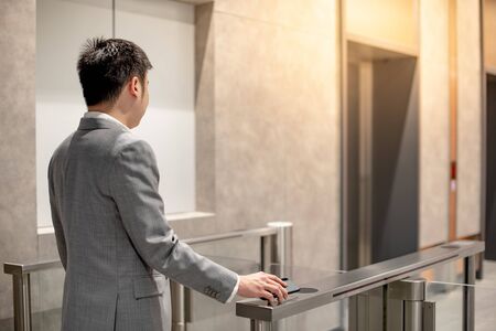 Asian businessman in formal business wear using smartphone to open automatic gate machine in office building. Working routine conceptの写真素材