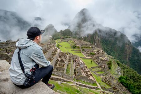 Young Asian man traveler and photographer looking at Machu Picchu, one of seven wonders and famous tourist attraction in Cusco Region of Peru. This majestic place has known as 'Lost City of the Incas'の写真素材