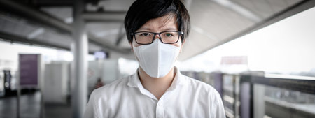Asian man wearing face mask at skytrain station or urban train platform.  coronavirus (COVID-19)...