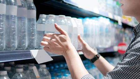 Male shopper picking pack of mineral water bottle from product shelf in supermarket. Customer shopping drinking water in grocery store. Healthy lifestyleの写真素材