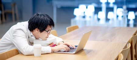 Young Asian man university student with glasses and headphones using laptop computer for online learning course at home. E-learning on internet during quarantine. Study from anywhere conceptの写真素材