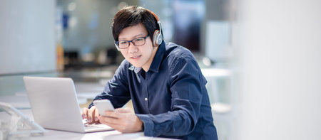 Smart Asian businessman in casual clothing using smartphone and laptop computer working at home office. Male manager using mobile app for social media and online news. Technology for business strategyの写真素材