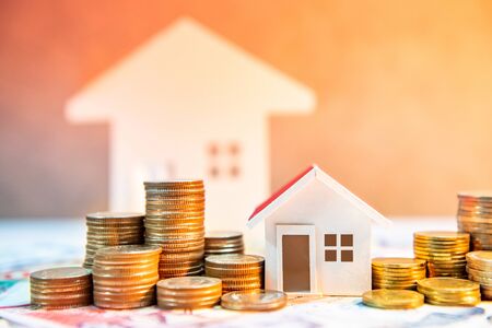 Real estate or property investment. Home mortgage loan rate. Saving money for retirement concept. Coin stack on international banknotes with house model on table. Business growth backgroundの写真素材