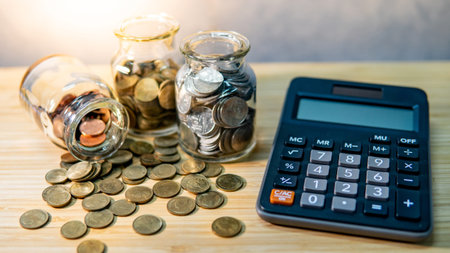 Calculator with coin in currency glass jar and spilling on wooden table. Compound interest rate...