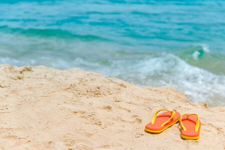 Orange flip flops or slippers on tropical island beach. Footwear for summer holiday or relaxing vacation. Summertime travel conceptの写真素材