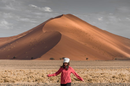 Asian woman traveler walking against dramatic sand dune desert landscape in Namib-Naukluft National Park, Namibia, Africaの写真素材