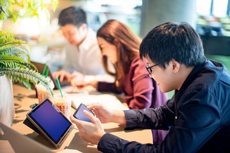 Asian businessman using smartphone and digital tablet while working with colleagues in green home office. Modern working lifestyle with portable smart device. Business meeting conceptの写真素材