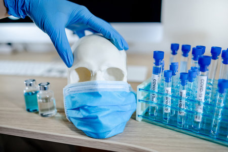Doctor hand in latex gloves holding human skull or cranium head wearing blue surgical mask with test...