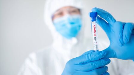 Medical scientist man in personal protective equipment suit (PPE), mask and gloves holding COVID-19 Test tube in hospital laboratory. Male doctor getting result of Coronavirus case. 2019-nCoV researchの写真素材